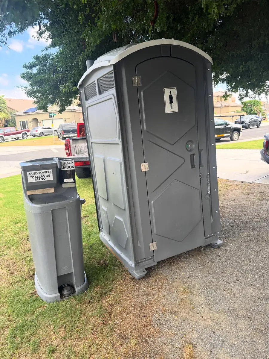 Grey porta potty with a separate hand-wash station on grass